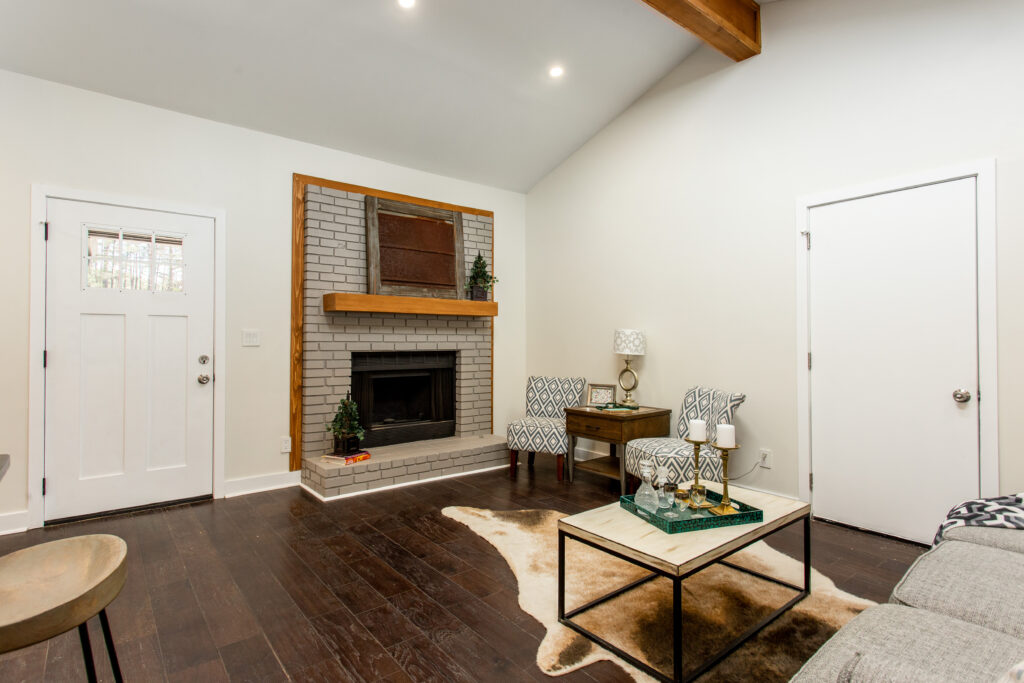 Open concept living and kitchen area featuring vaulted ceilings with exposed wood beams, a stone fireplace, kitchen island with seating, and dark hardwood floors, home renovation by Parsons Mission Construction