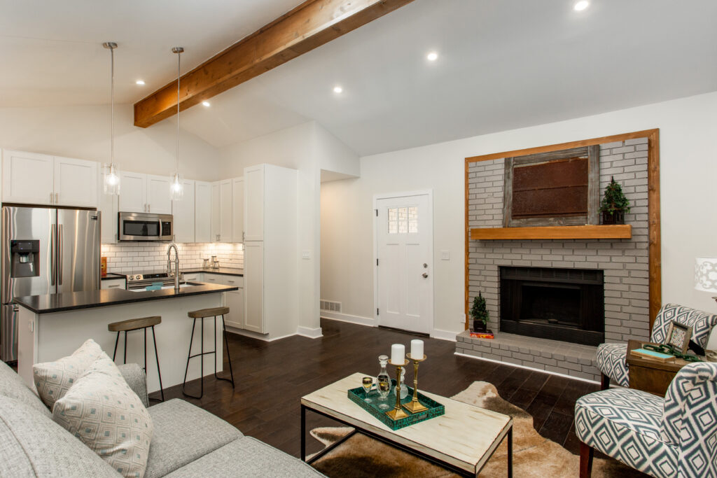 Open living and dining area featuring a stone fireplace, exposed wood ceiling beams, vaulted ceilings, and dark hardwood floors, home renovation by Parsons Mission Construction