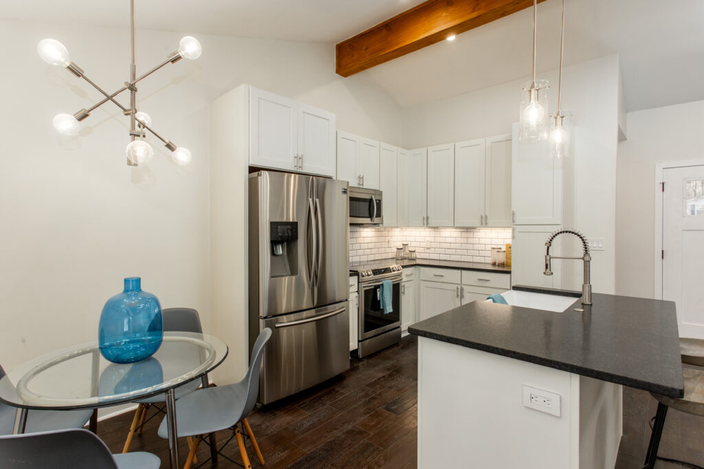 Open concept kitchen and living area featuring exposed wood ceiling beams, vaulted ceilings, stainless steel appliances, and dark hardwood floors, home renovation by Parsons Mission Construction