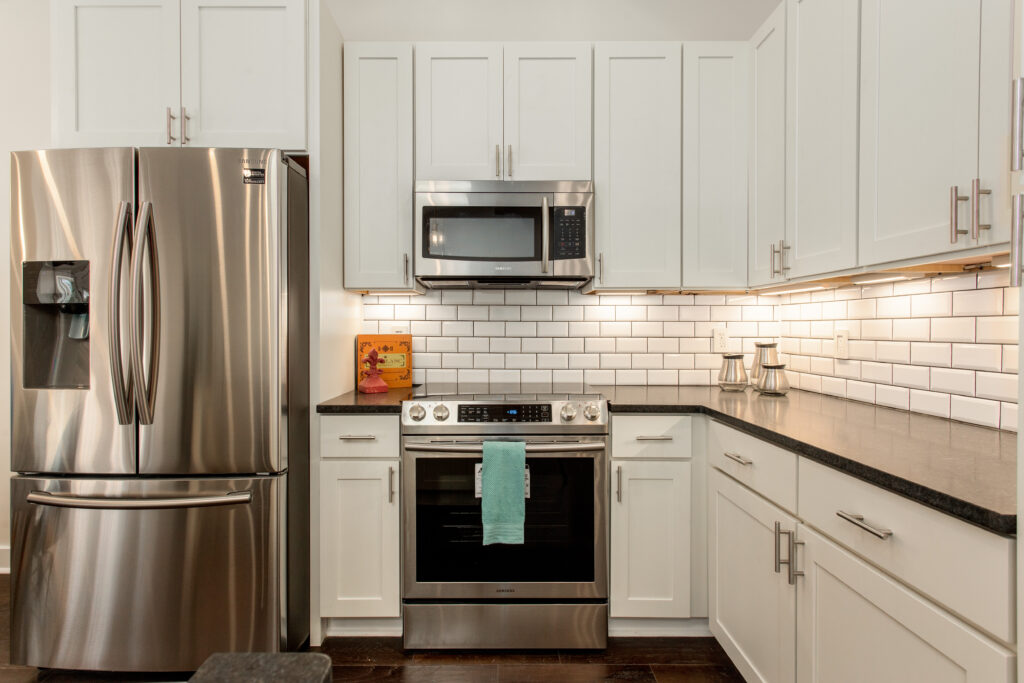 Renovated kitchen featuring white cabinetry, subway tile backsplash, stainless steel appliances including a refrigerator and microwave, and dark hardwood floors, kitchen remodeling by Parsons Mission Construction