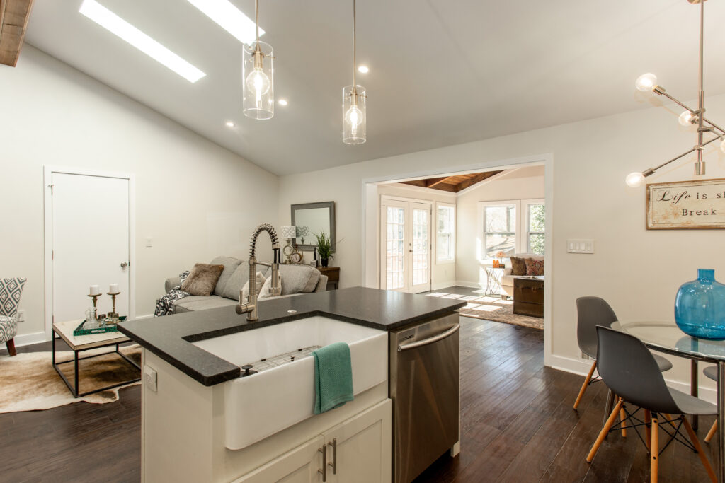 Open concept living and kitchen area featuring white cabinetry, dark countertops, pendant lighting, dark hardwood floors, and a comfortable seating area, home renovation by Parsons Mission Construction