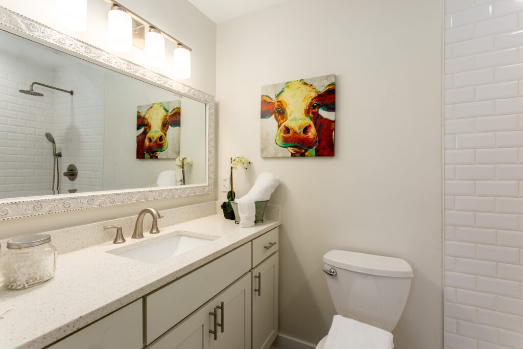 Renovated bathroom featuring a gray vanity with white countertop, a large mirror with light bar, and decorative wall art, bathroom remodeling by Parsons Mission Construction