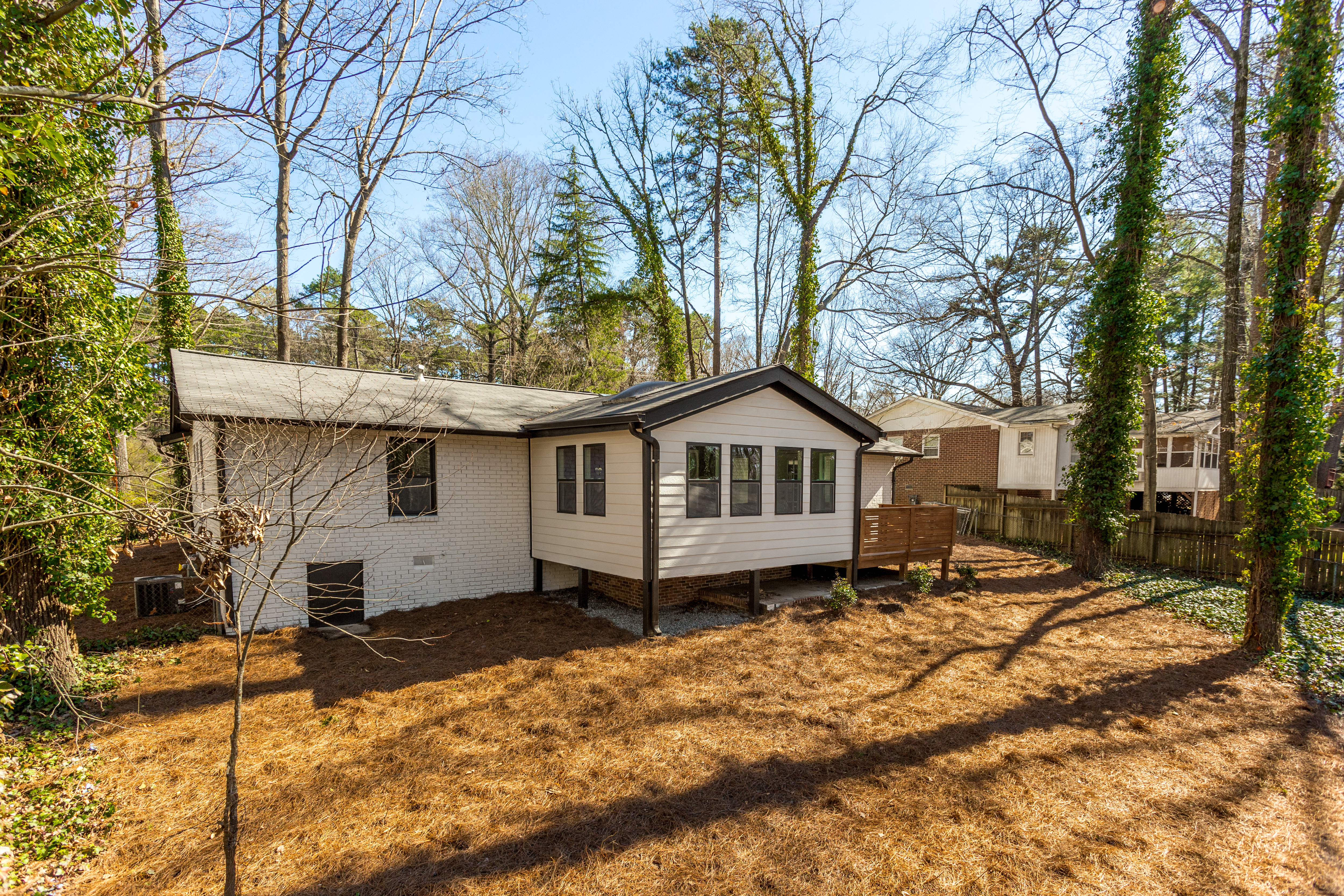 Side view of a renovated home featuring white siding, a wood deck, and mature trees in the surrounding yard, exterior renovation by Parsons Mission Construction