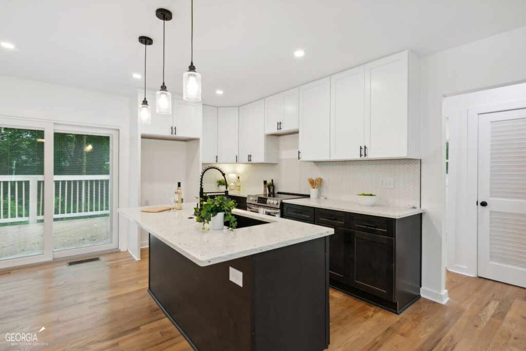 Renovated kitchen featuring a dark center island with granite countertop, white upper cabinets, herringbone tile backsplash, pendant lighting, hardwood floors, and a sliding glass door to an outdoor deck, kitchen remodeling by Parsons Mission Construction