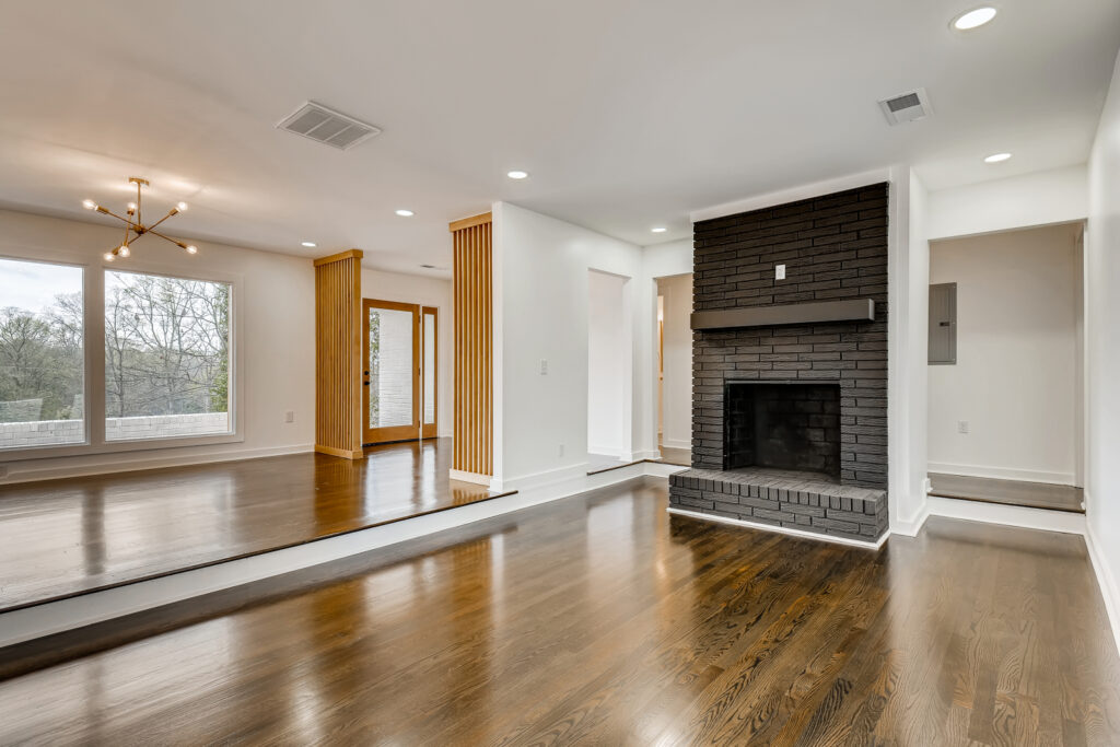Renovated living room featuring a stone fireplace, wood accent wall, hardwood floors, and large windows with natural light, home renovation by Parsons Mission Construction