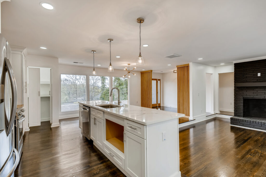 Open concept kitchen and living area featuring white cabinetry, a large island, hardwood floors, and a chandelier, with a beautiful fireplace and wooden features home renovation by Parsons Mission Construction