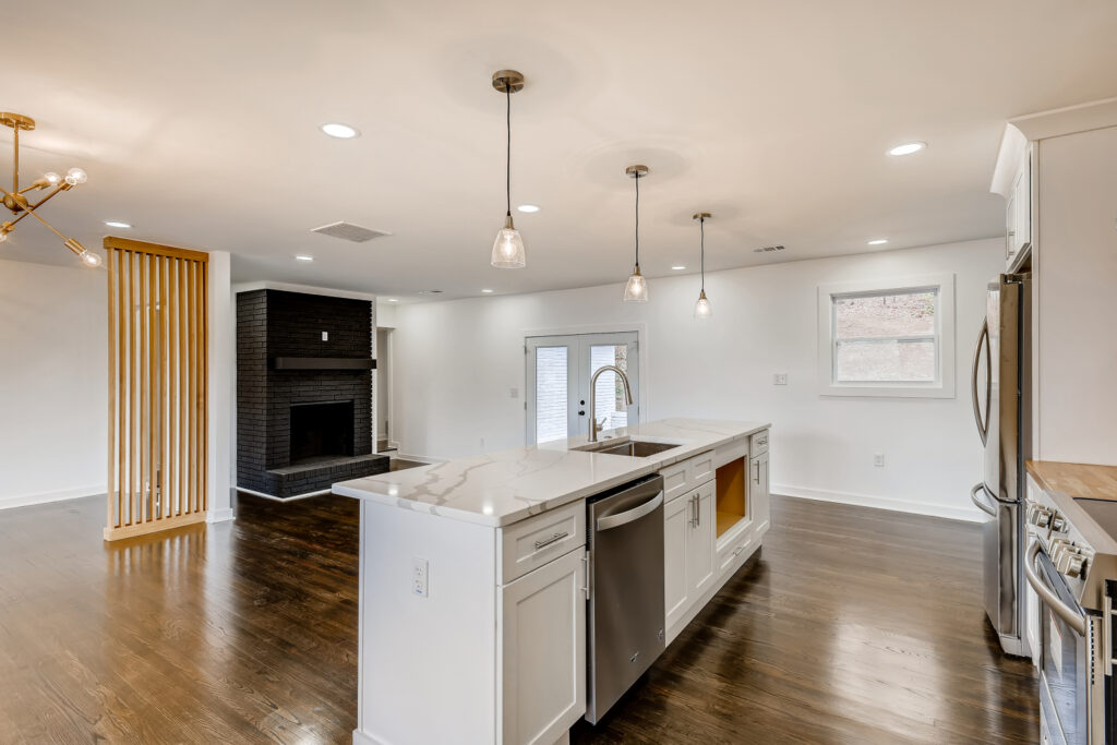 Open concept kitchen featuring a large white island with marble countertop, pendant lighting, dark hardwood floors, and black appliances, kitchen remodeling by Parsons Mission Construction