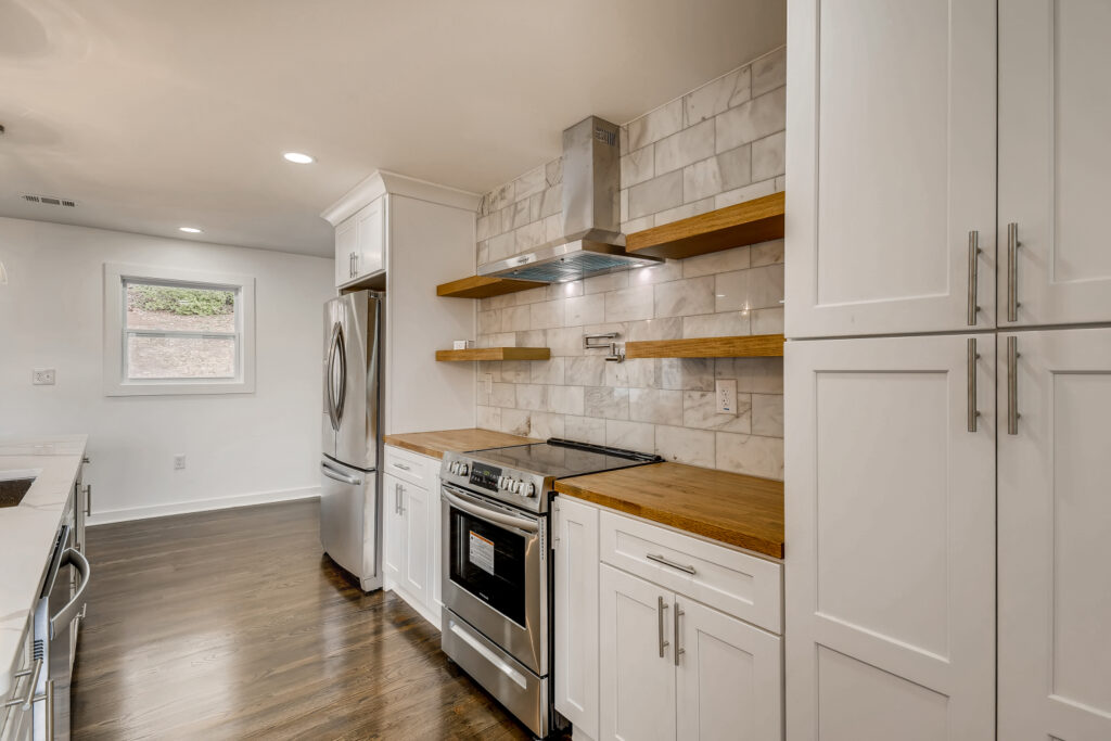 Renovated kitchen featuring white cabinetry, open wood shelving, subway tile backsplash, a stainless steel range, and dark hardwood floors, kitchen remodeling by Parsons Mission Construction