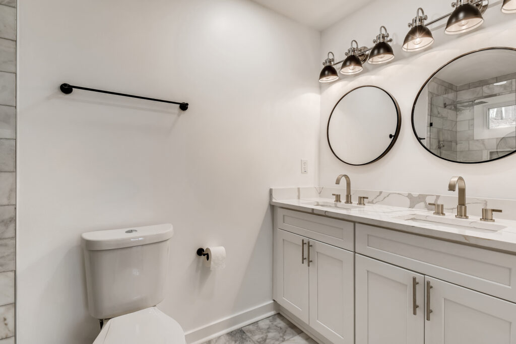 Renovated bathroom featuring a gray double vanity, round mirrors, white walls, and modern light fixtures, bathroom remodeling by Parsons Mission Construction