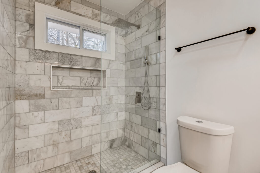 Walk-in shower featuring floor-to-ceiling marble tile surround, a built-in niche, rainfall showerhead, frameless glass enclosure, and a window for natural light, bathroom remodeling by Parsons Mission Construction