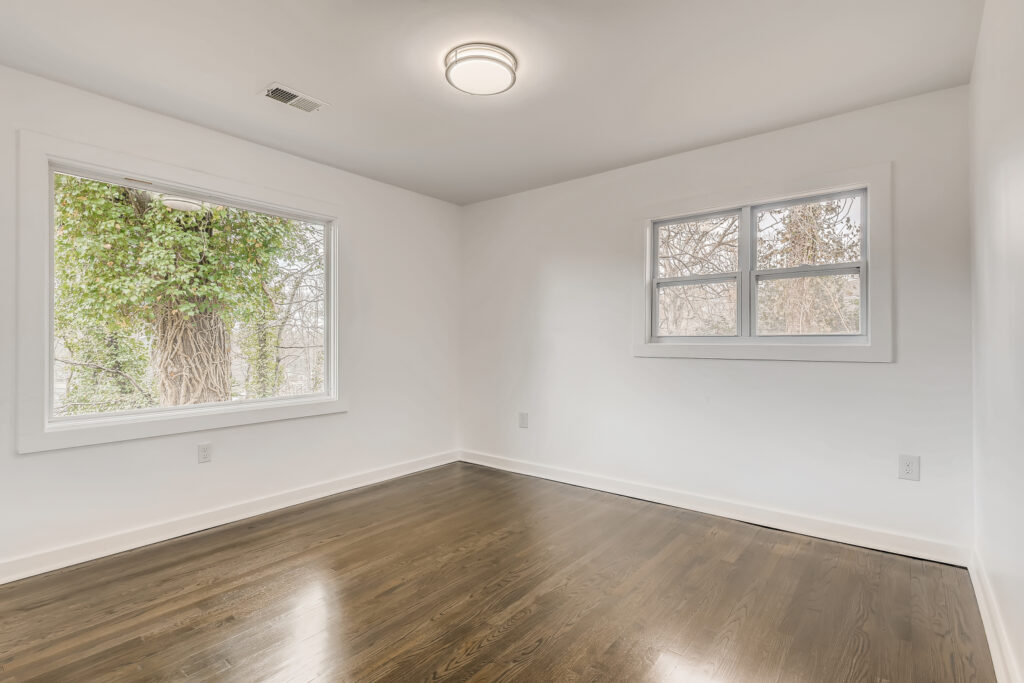 Freshly renovated interior room featuring dark hardwood floors, white walls, and large windows offering views of mature trees and natural light, home renovation by Parsons Mission Construction