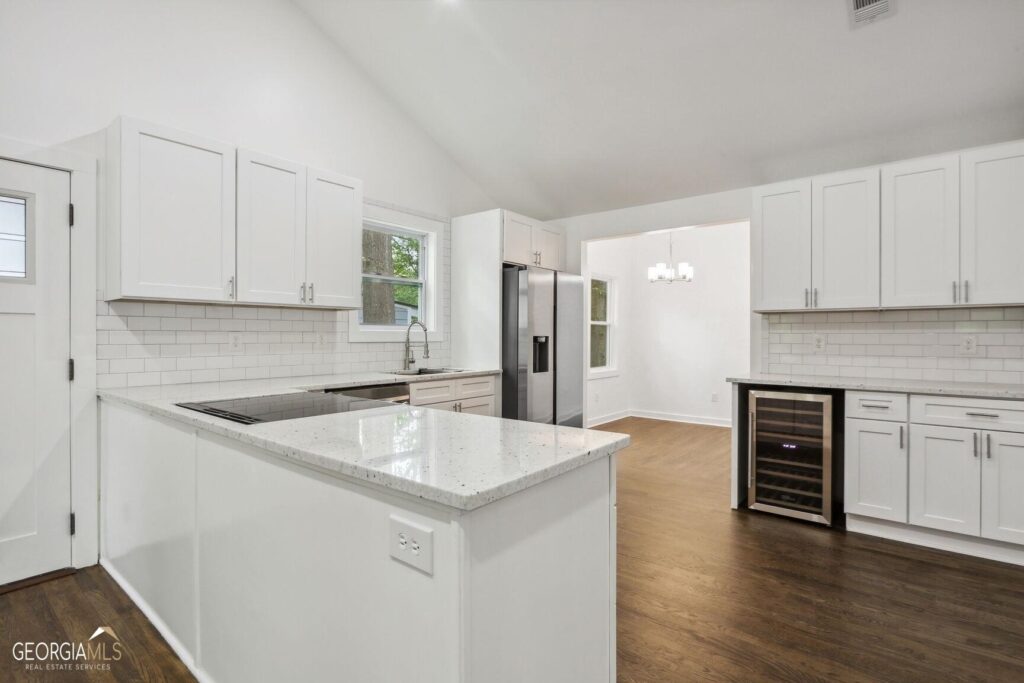 Renovated kitchen featuring white shaker cabinets, granite countertop island, subway tile backsplash, dark hardwood floors, stainless steel refrigerator, and a built-in wine cooler, kitchen remodeling by Parsons Mission Construction