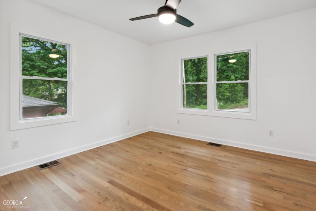 Renovated interior room featuring refinished hardwood floors, fresh white walls, large windows with natural light, and a ceiling fan, home renovation by Parsons Mission Construction