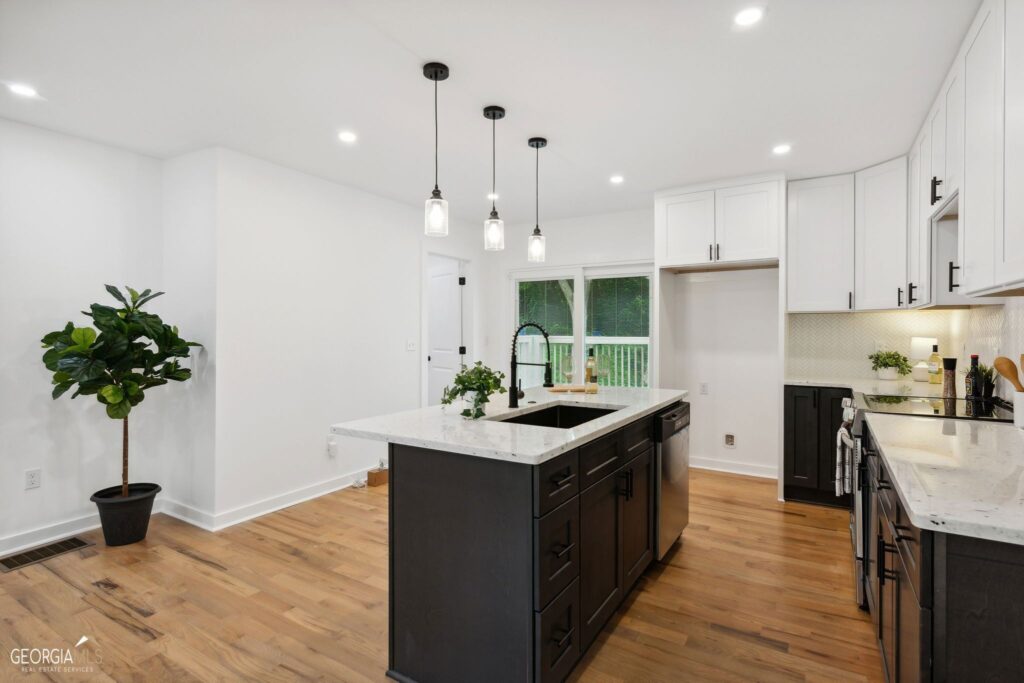 Open-concept kitchen featuring a dark island, pendant lighting, white cabinetry, and hardwood floors leading to an adjacent room, kitchen remodeling by Parsons Mission Construction