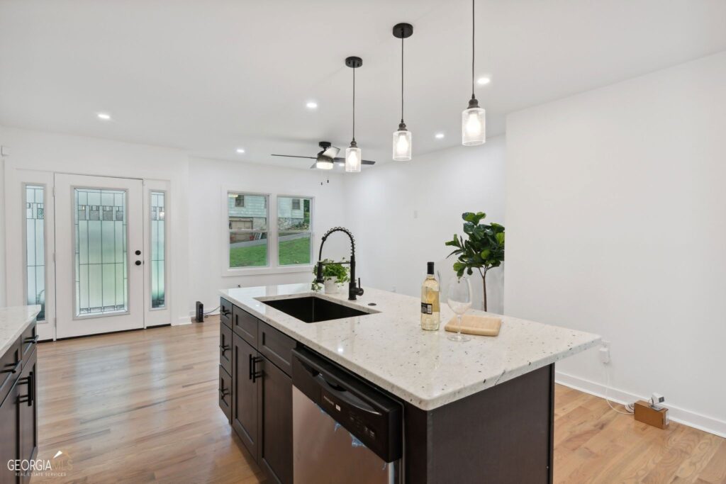 Renovated kitchen featuring a dark center island with white countertop, pendant lighting, white cabinetry, and hardwood floors, kitchen remodeling by Parsons Mission Construction