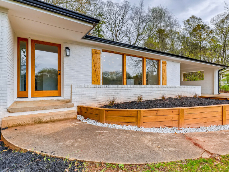 Front exterior of a mid-century modern home with white walls, wood accents, and a landscaped front yard, exterior renovation by Parsons Mission Construction