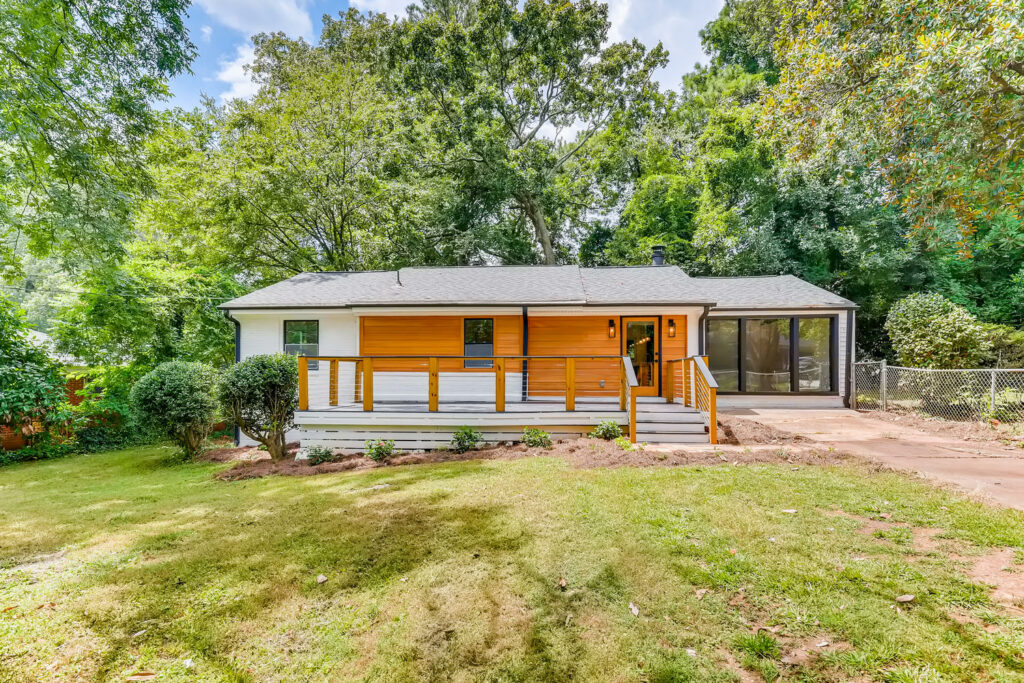 Front exterior of a home featuring wood siding, a covered front porch, and a well-maintained green lawn surrounded by mature trees, exterior renovation by Parsons Mission Construction