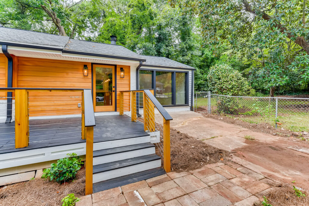 Renovated home exterior featuring a wood deck, wood railings, and lush green landscaping with mature trees, exterior renovation by Parsons Mission Construction